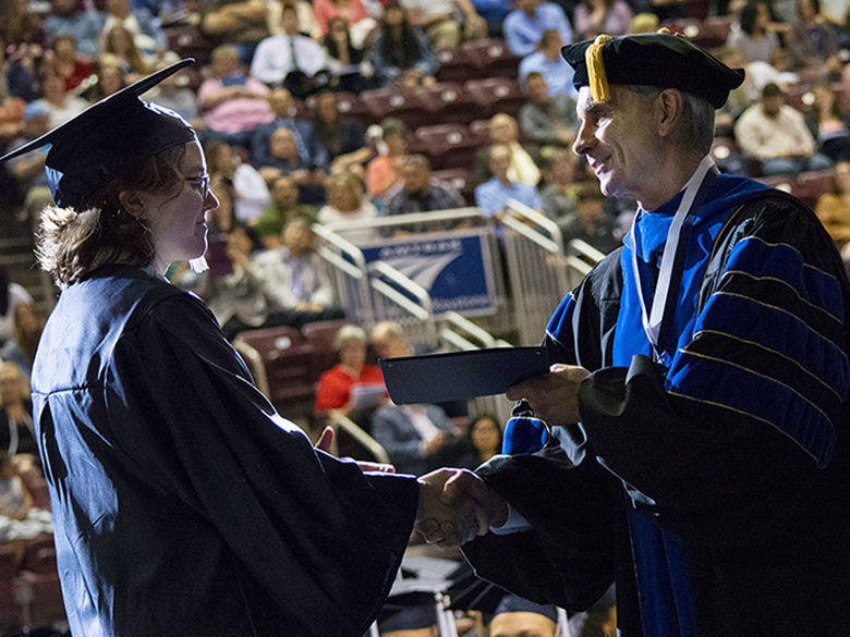 A graduate receives their degree while shaking hands with the Chancellor
