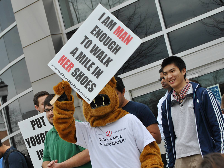 The Nittany Lion mascot holding a Walk A Mile in Her Shoes sign