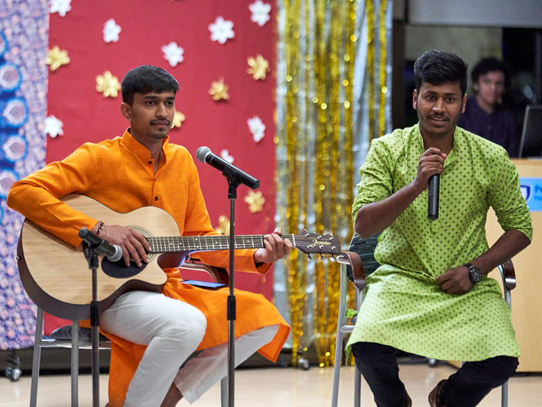 Two international students perform at Diwali, playing guitar and singing